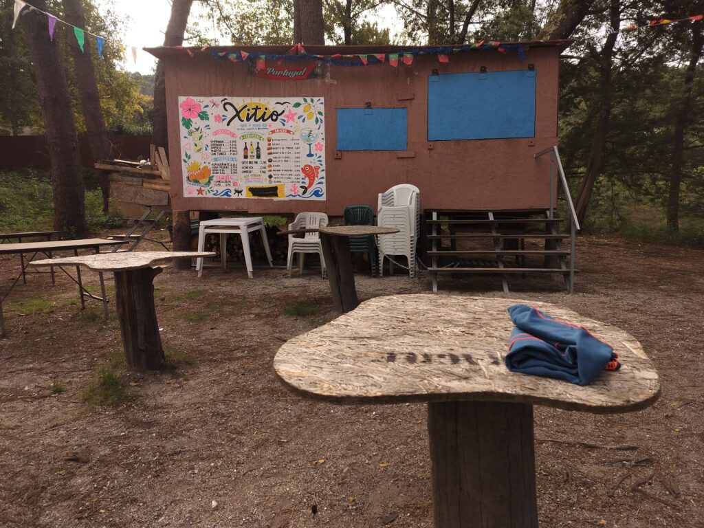 Tables cut from irregular boards on wooden posts in front of the bar, with a folded blue cloth on one of them.